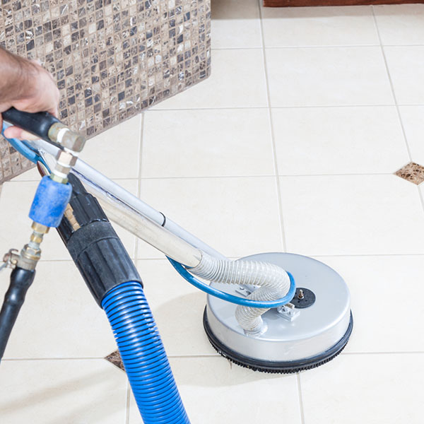 Man cleaning tile and grout with machine in bathroom